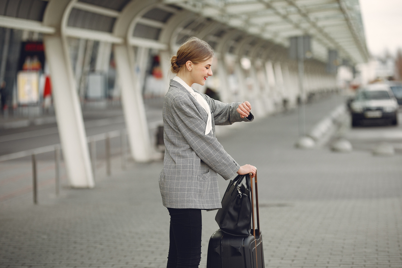 Cheerful female manager checking time on wristwatch standing with bags near bus station
